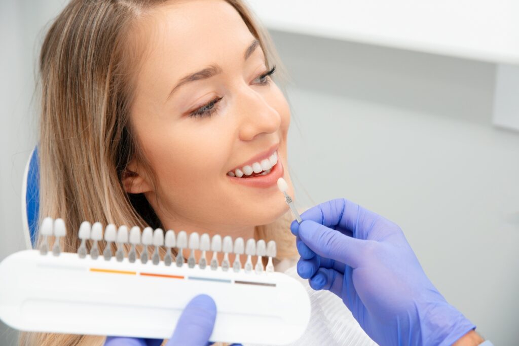 Dental professional in blue gloves showing patient tooth shade guide for cosmetic dentistry consultation.