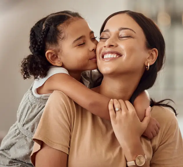 Young child hugging smiling mother from behind in warm home setting.